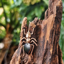 Load image into Gallery viewer, Meat‑ant–inspired earring made from black car vinyl with recycled copper body segments, a sterling‑silver hook, and hypoallergenic stainless‑steel jump rings, shown hanging on textured wood with soft green foliage in the background.