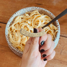 Load image into Gallery viewer, FEED ME ear cuff modelled on Sheridan Eveline's hand in front of a bowl of pasta