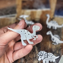 Load image into Gallery viewer, Hand holding a velociraptor dinosaur hoop earring with more dinosaurs in the background
