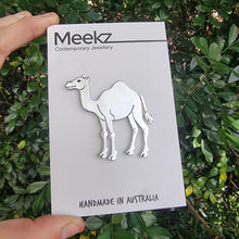 Load image into Gallery viewer, Card with camel brooch featuring hand stamped details held up in front of a bush with lots of leafy branches
