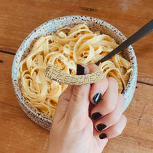 Load image into Gallery viewer, FEED ME ear cuff modelled on Sheridan Eveline&#39;s hand in front of a bowl of pasta
