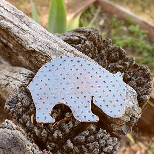 Copper wombat brooch sitting on a wooden fence